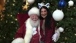A woman is posing for a picture with santa claus in front of a christmas tree.