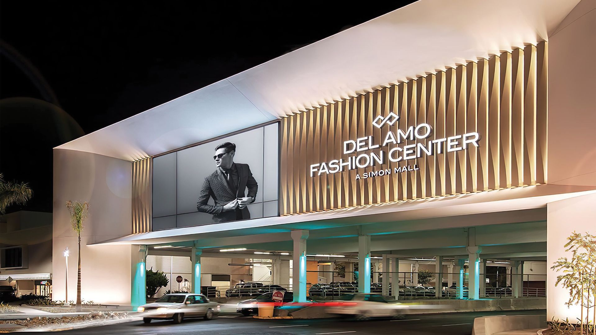 Del Amo Fashion Center entrance at night with illuminated sign and cars driving.
