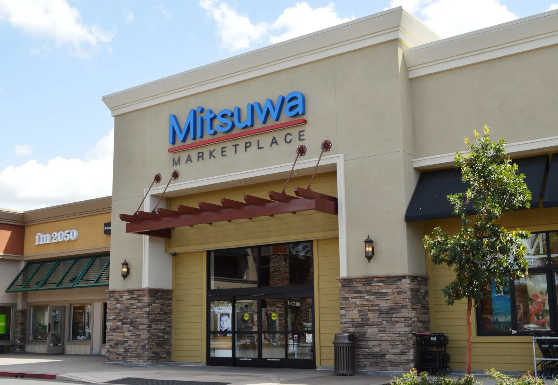 Mitsuwa Marketplace entrance. Beige building with blue sign, stone accents, and glass doors.