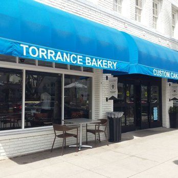 Torrance Bakery storefront with a blue awning, tables, and a black door.