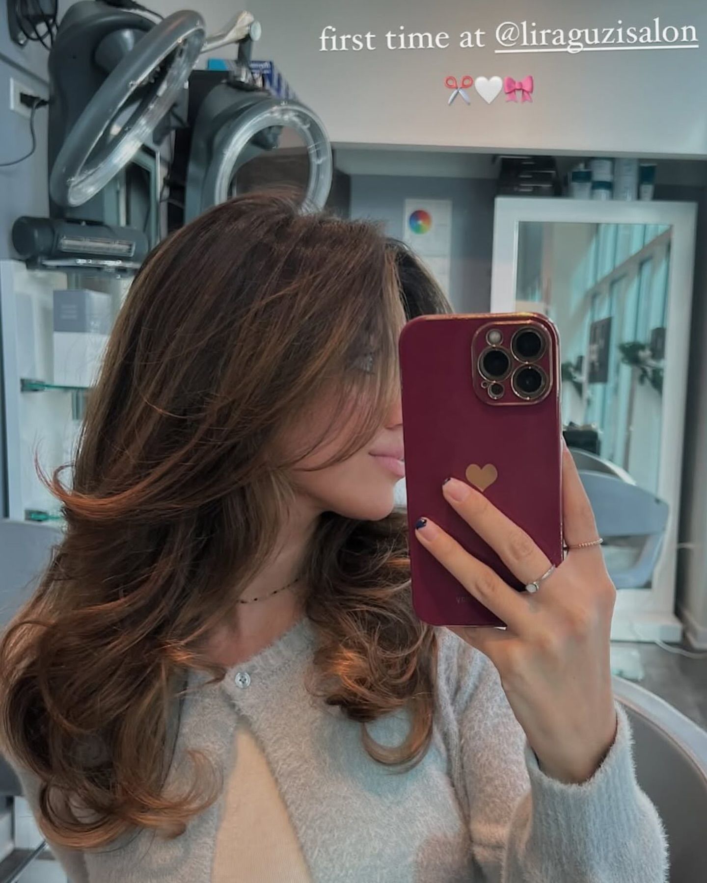 Woman with wavy brown hair, highlighted with lighter tones, in a salon setting.
