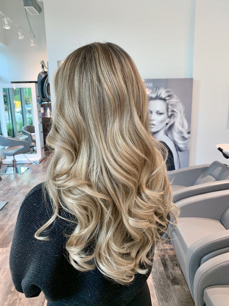 Woman with long, wavy blonde and light brown highlighted hair at a salon.