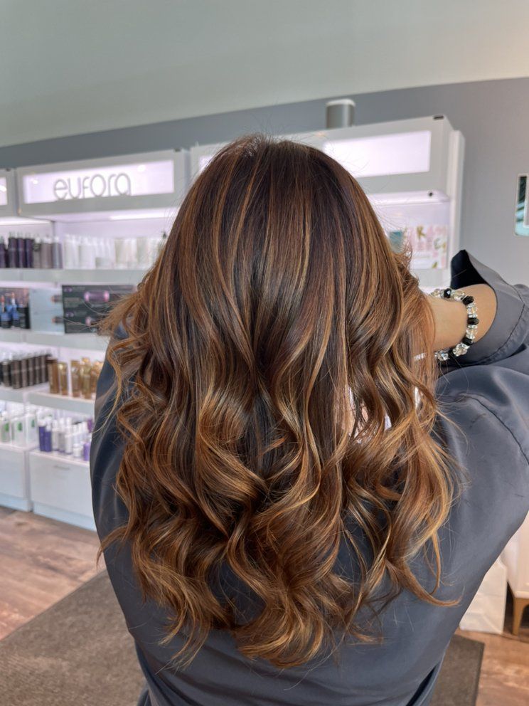 Woman with wavy brown hair, highlighted with lighter tones, in a salon setting.
