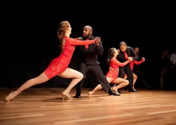 Dancers in red dresses and black suits performing on a wooden stage.