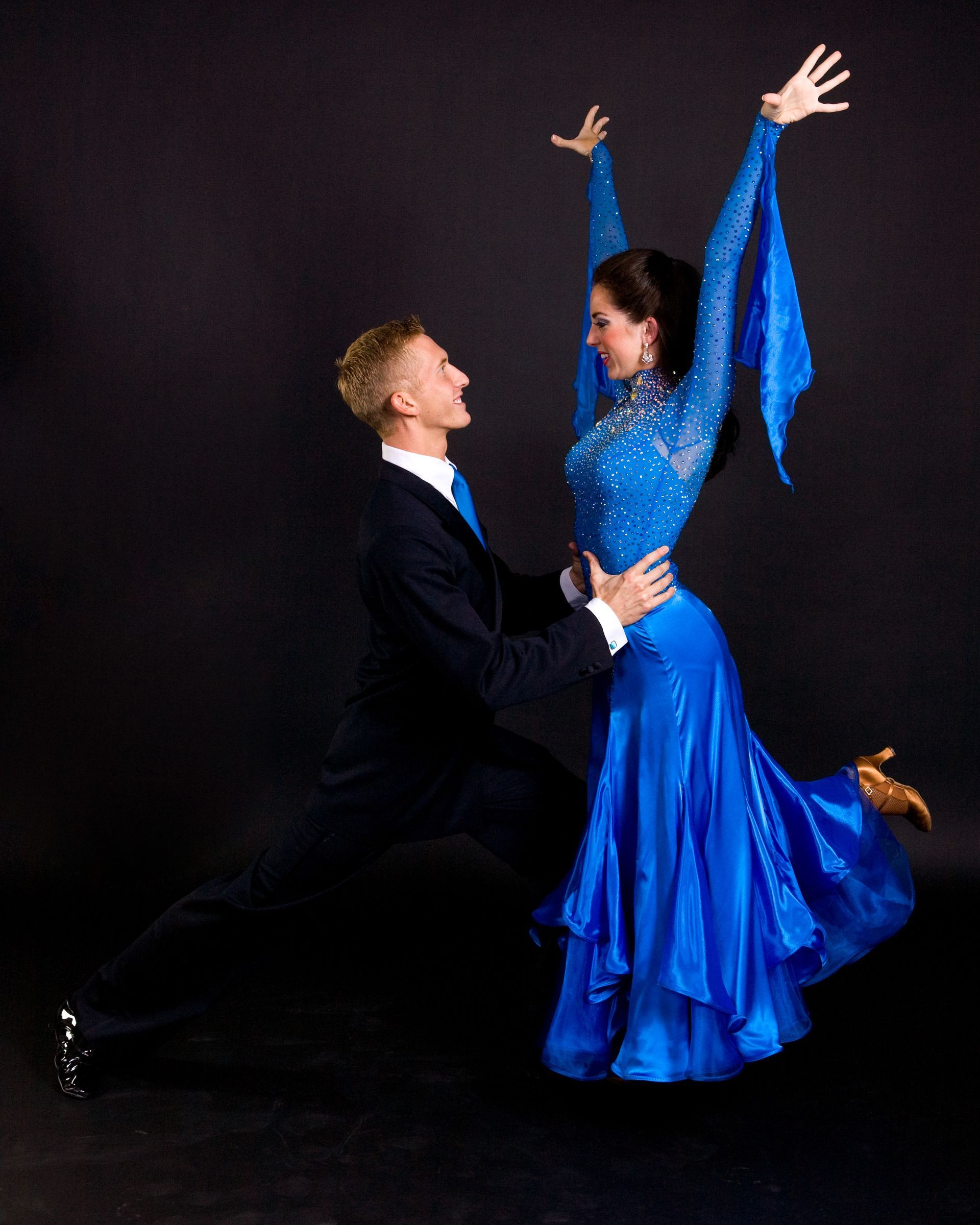 Man and woman in formal wear dancing, she in blue dress, he in black suit, both smiling.