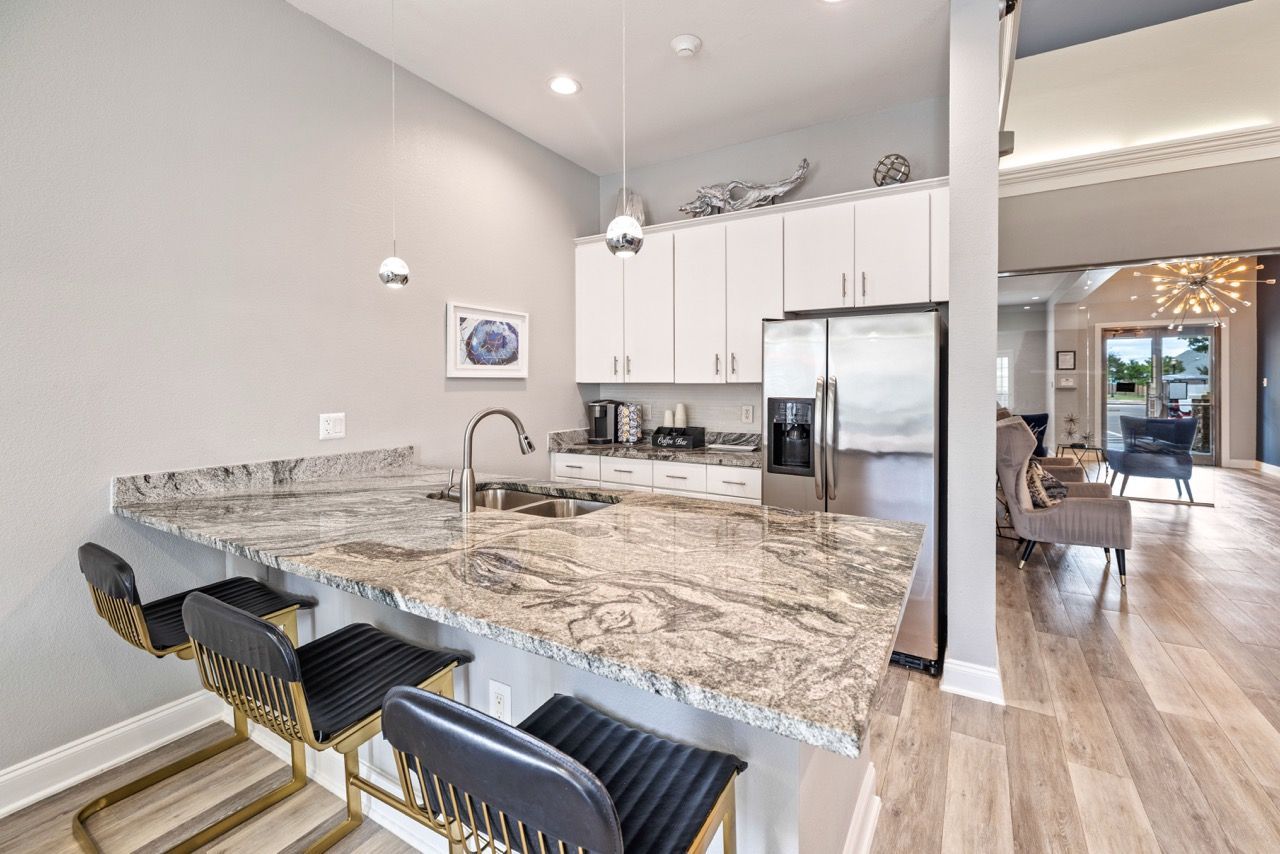 Open-concept kitchen with a granite island, stainless steel refrigerator, and bar stools.