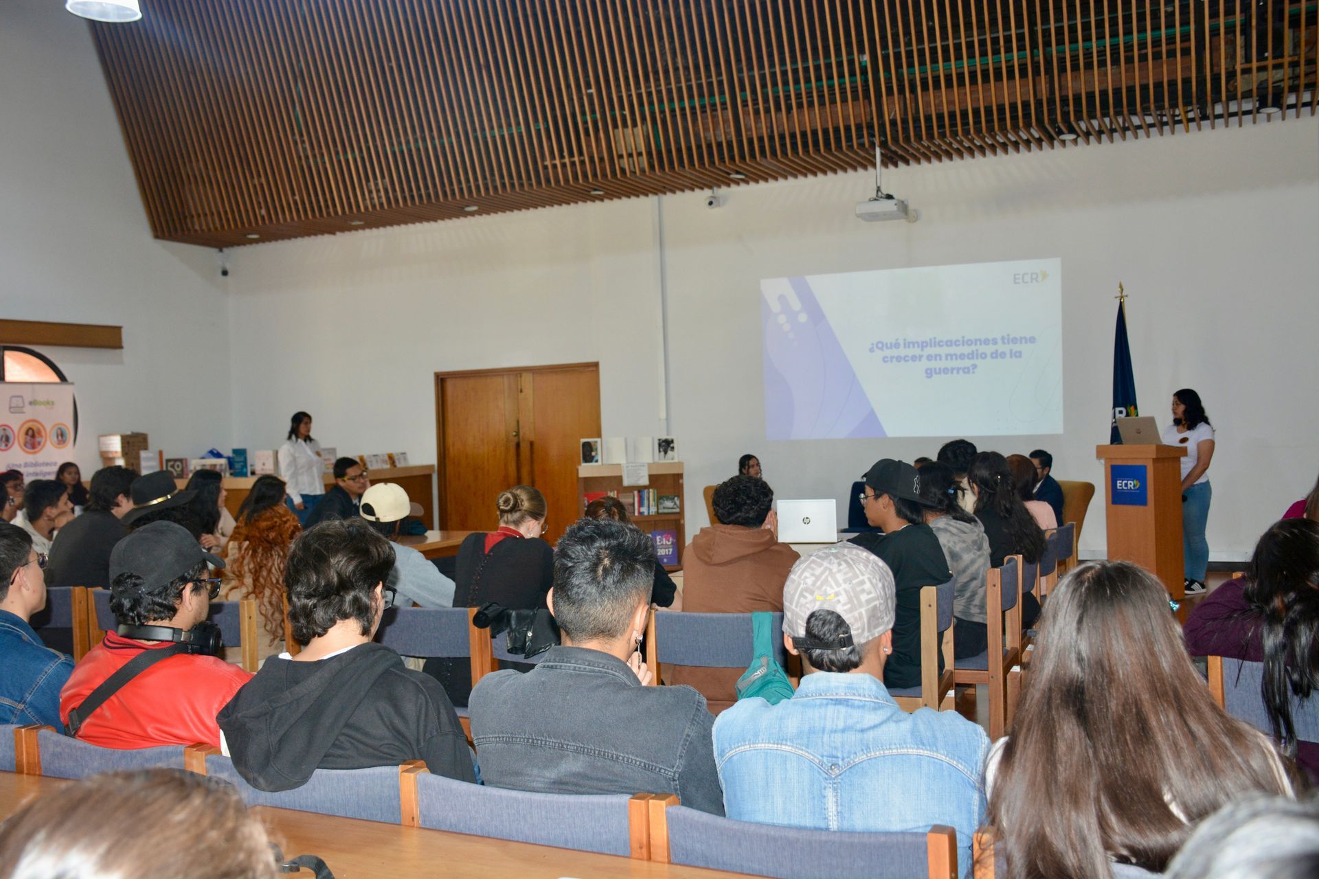 A group of people are sitting in a lecture hall watching a presentation.