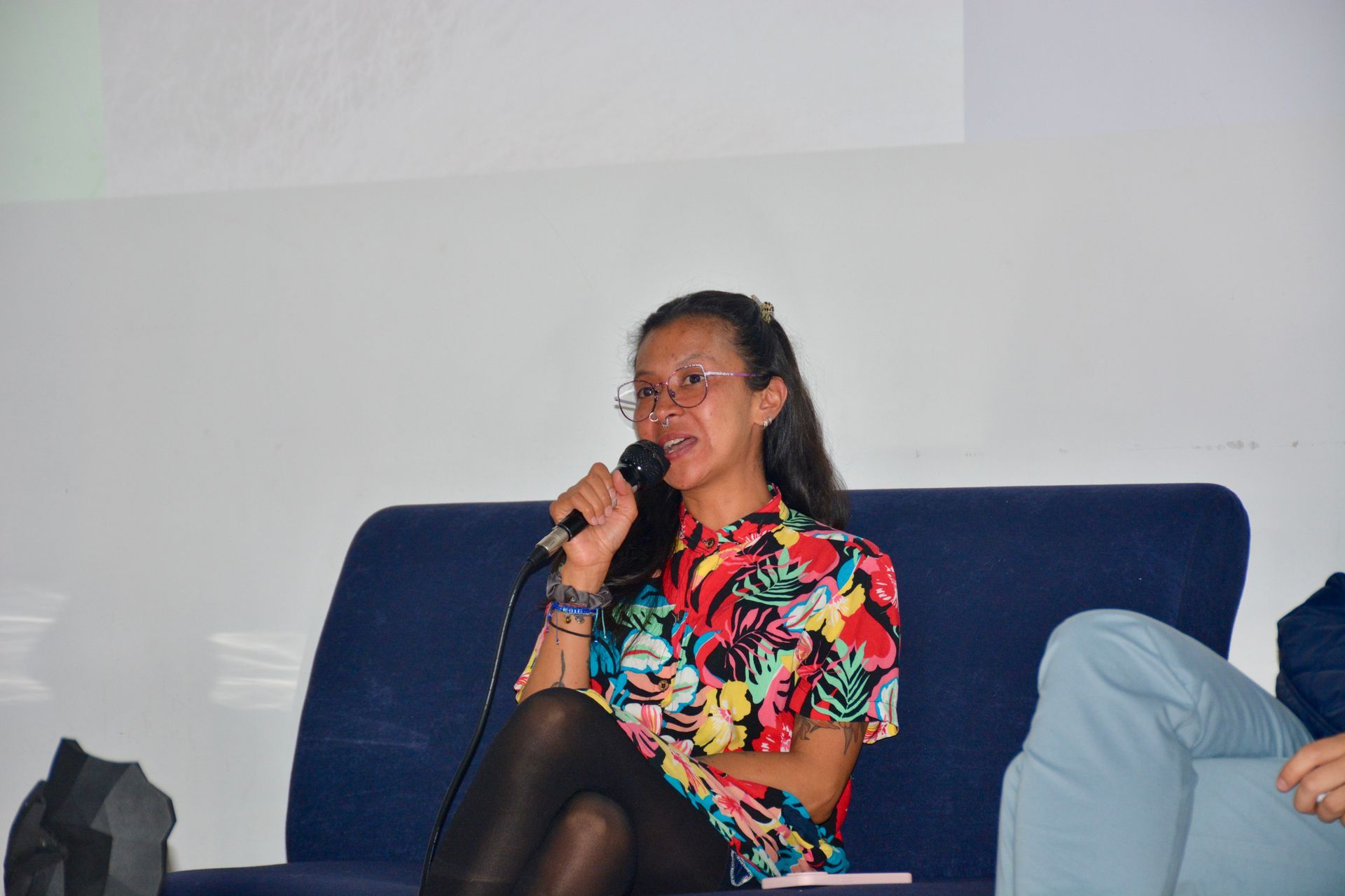 A woman is sitting on a couch talking into a microphone.