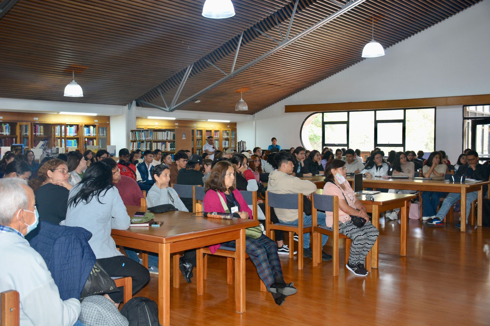 A large group of people are sitting at tables in a library.