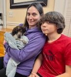 Woman in purple holding puppy; boy in red shirt beside her. All looking at the camera.