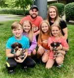 Family of six with puppies posing outside.