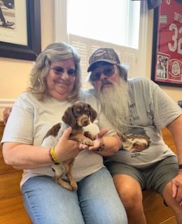 Woman and man with a puppy, smiling.  They are indoors.  The puppy is brown and white.