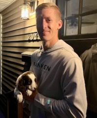 Man in gray hoodie holding puppy on porch, number 