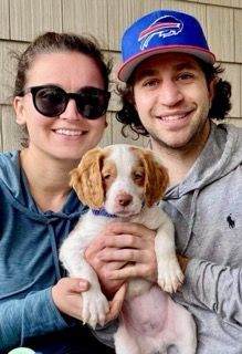 Woman and man holding a puppy. The man wears a Bills hat. All three smiling.