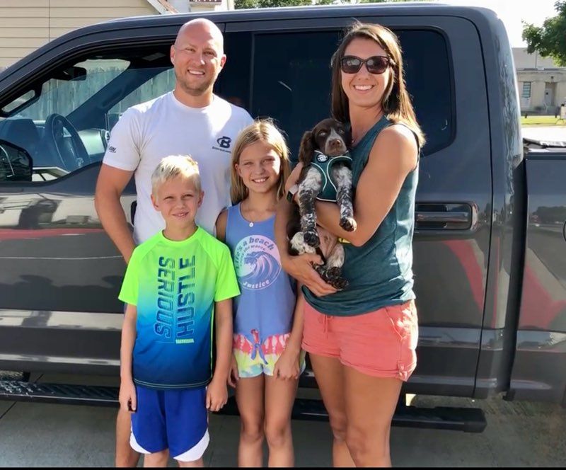 Family of four with a dog, posing in front of a gray pickup truck.