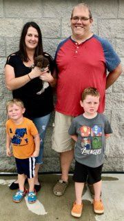 Family of five poses outdoors with a small puppy.