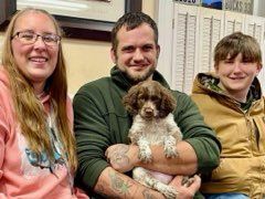 Family smiles holding a puppy in a room with white paneled wall.