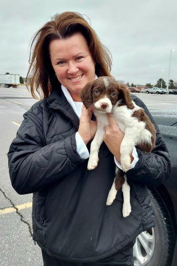 Woman holding a brown and white puppy outside, smiling.