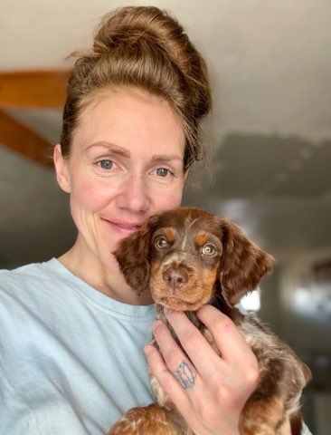 Woman holding a small brown and white puppy, smiling.