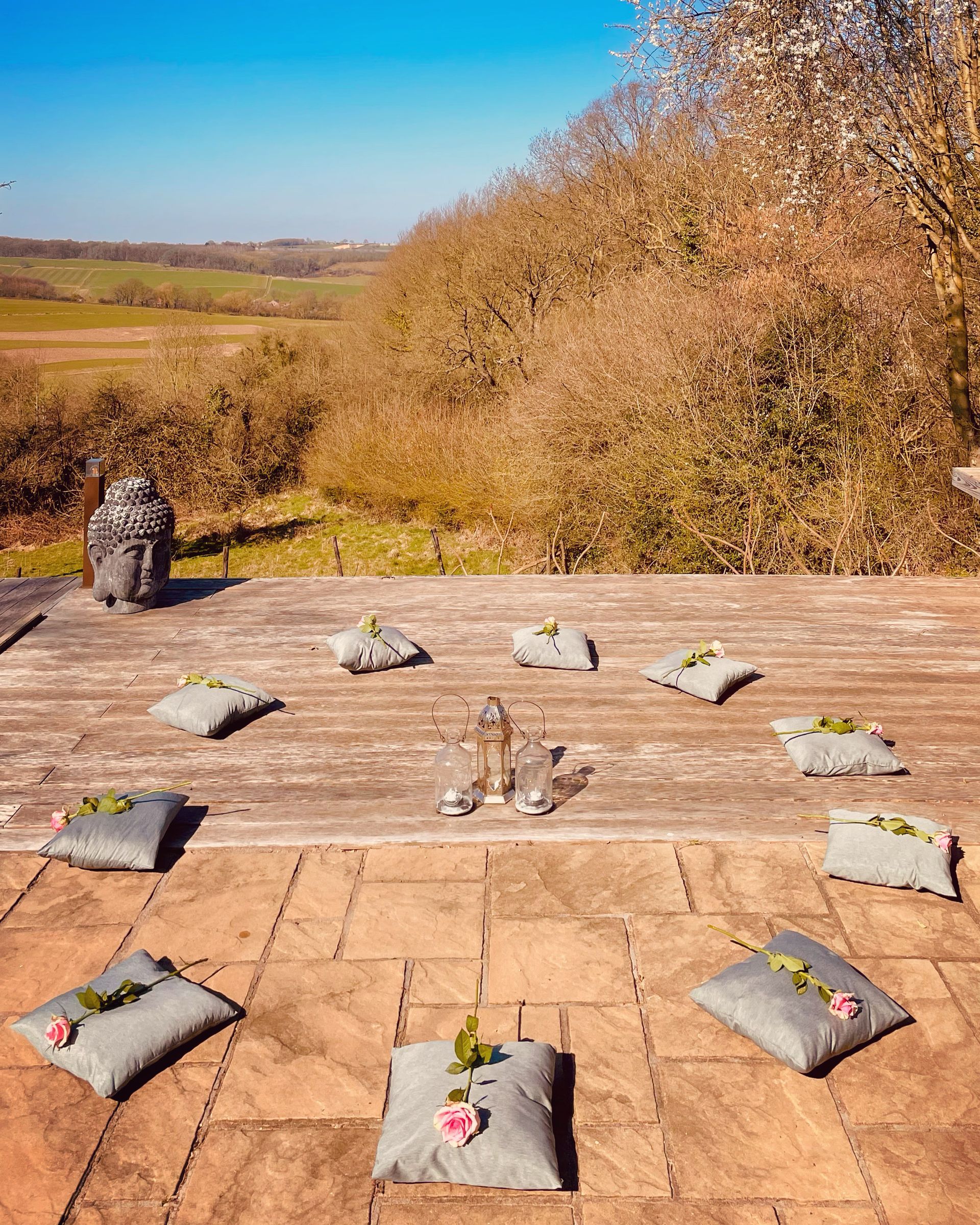 Outdoor meditation setting: cushions arranged in a circle, overlooking a landscape with blue sky.