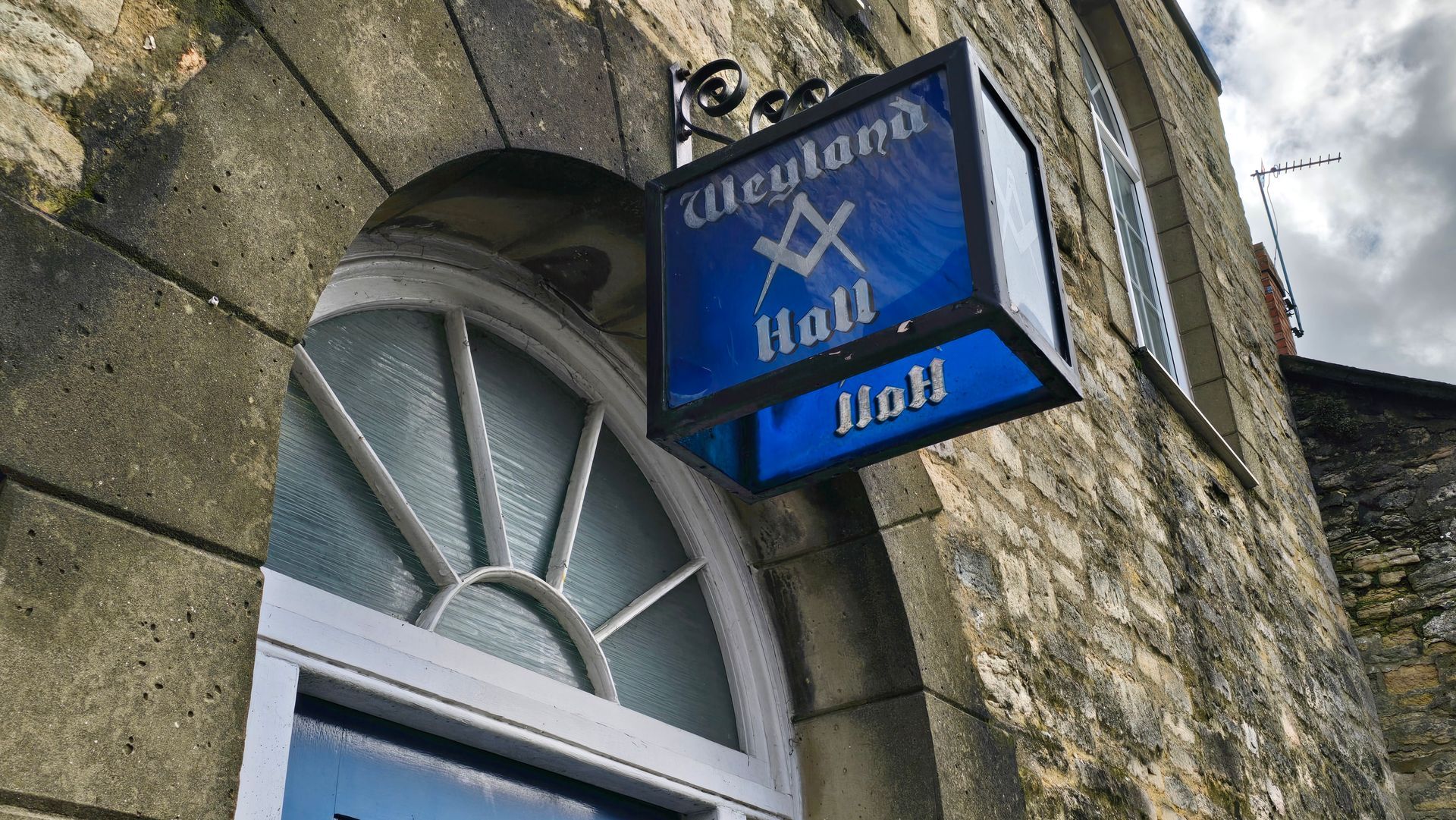 A blue sign is hanging from the side of a building.