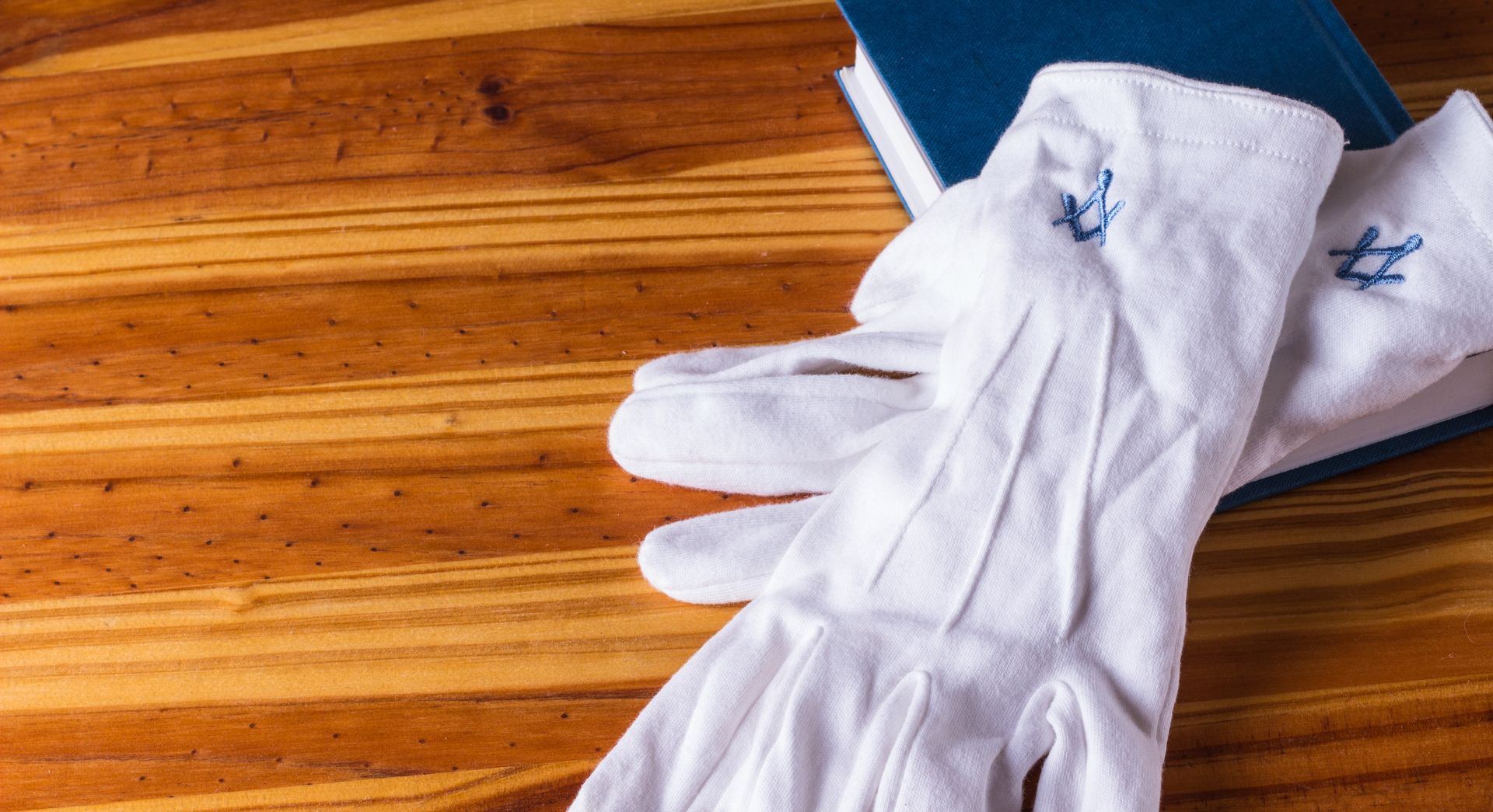 A pair of white masonic gloves are sitting on a wooden table next to a book.