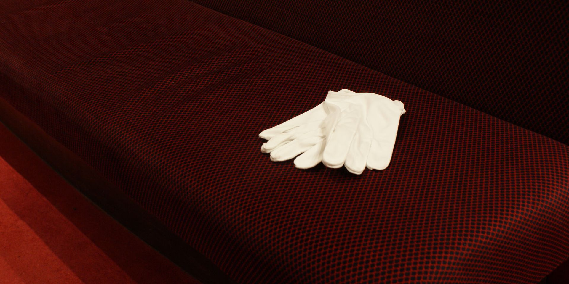 A pair of white gloves are sitting on a red couch.