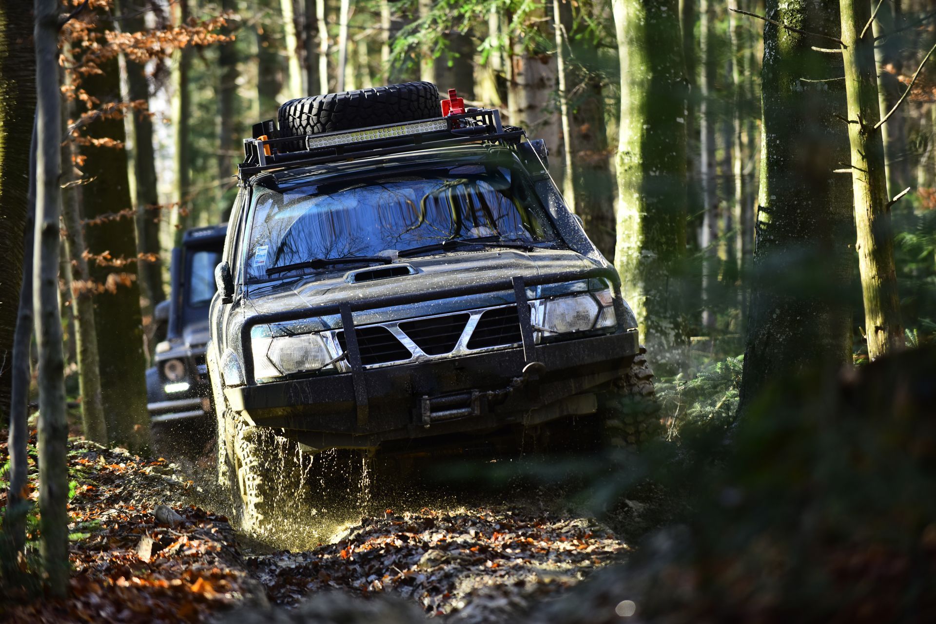 Two sport utility vehicles or SUVs overcome obstacles in a motor race in an autumn forest.