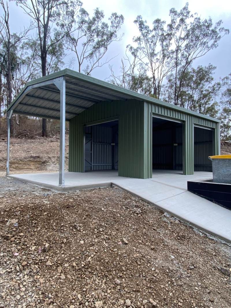 A Green Metal Garage With A Canopy Is Sitting On Top Of A Dirt Hill — Shed Constructions (QLD) In Gin Gin, QLD