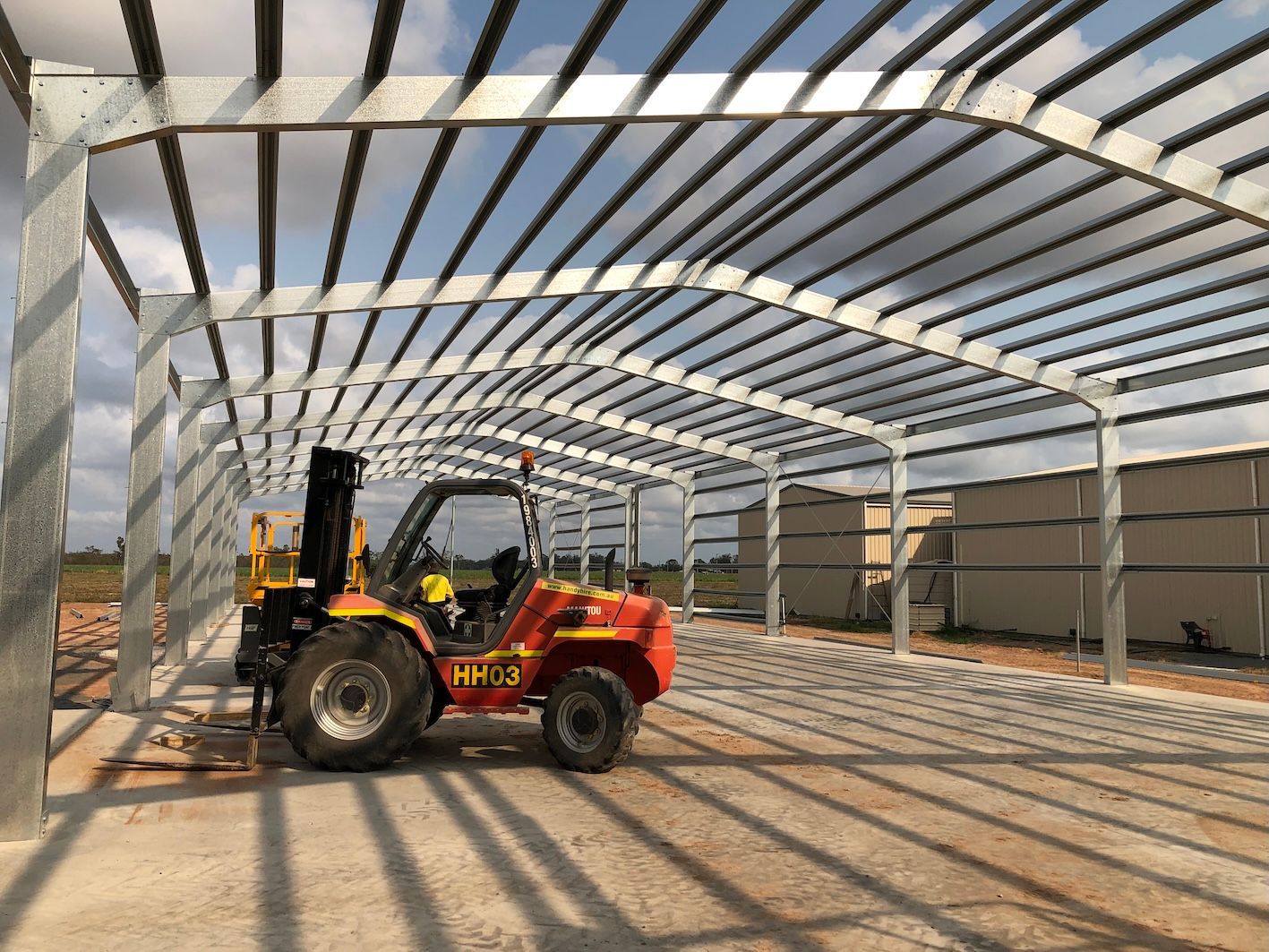 A yellow and red forklift in a metal frame building under construction, beams overhead - Shed Constructions (QLD) In Gin Gin, QLD