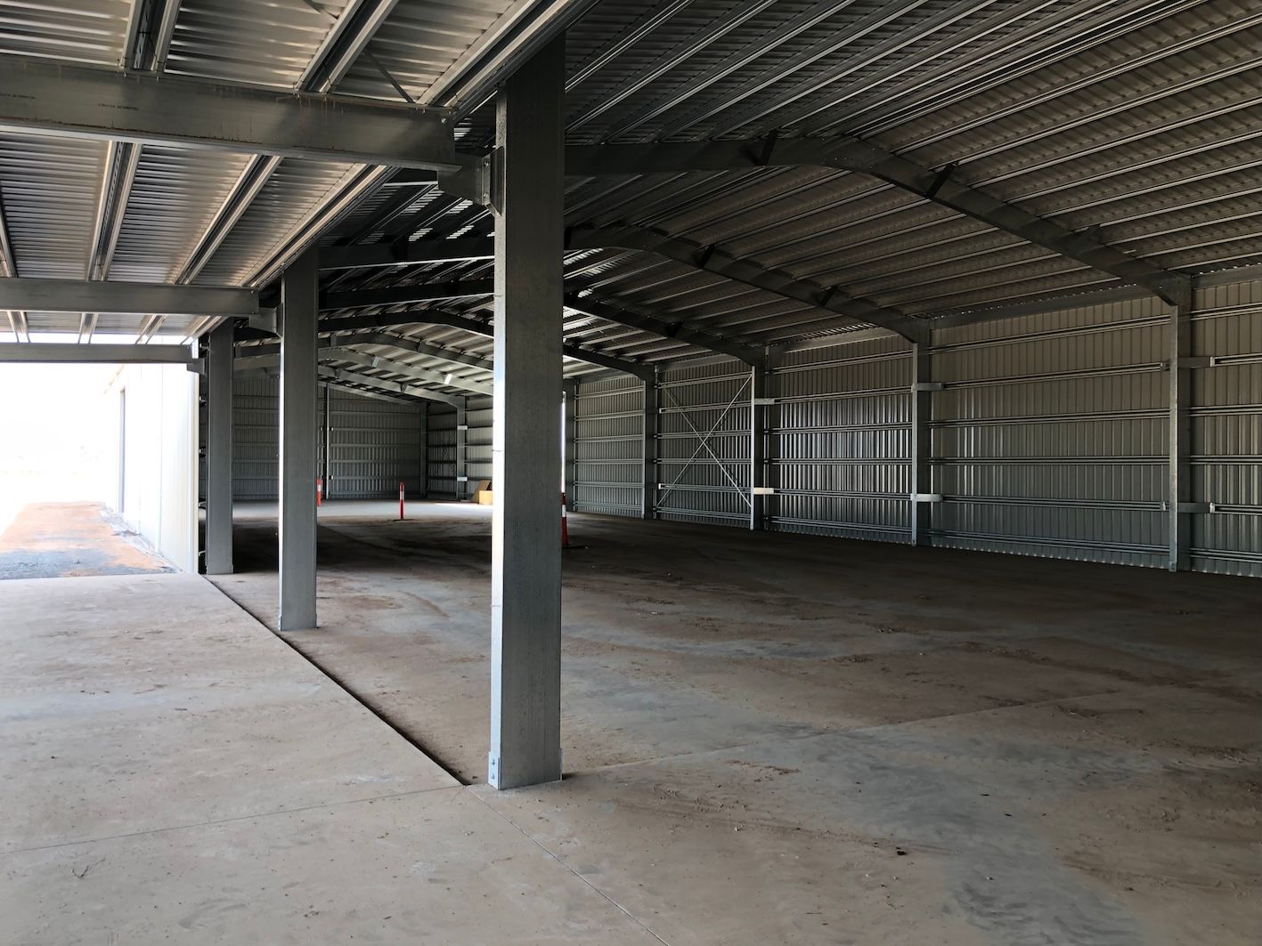 Interior of a large, empty metal building with concrete floor and support beams.