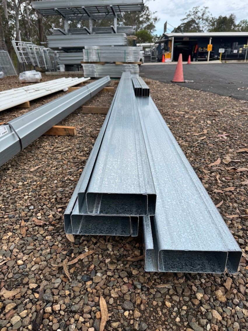 Metal beams stacked outdoors on gravel. Various sizes, gray -— Shed Constructions (QLD) In Gin Gin, QLD
