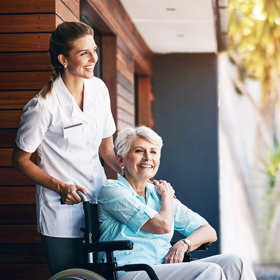 A nurse is standing next to an elderly woman in a wheelchair.