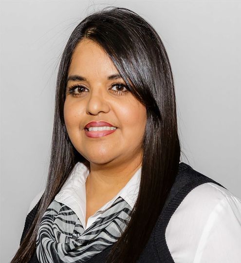 Woman in black suit smiles at the camera against a grey backdrop.