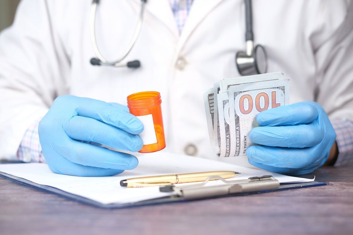 Doctor holding prescription bottle and cash, wearing gloves, stethoscope around neck.