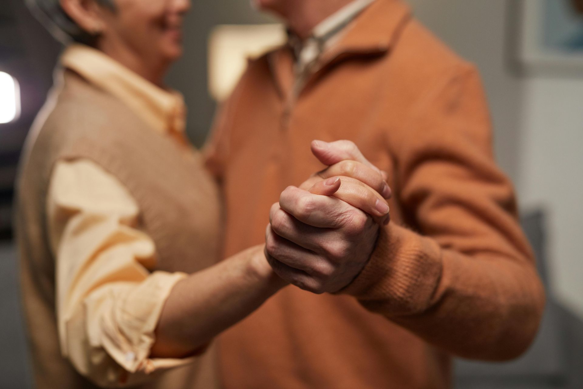 Elderly couple dancing closely, holding hands. Man in orange sweater, woman in tan vest smiling.