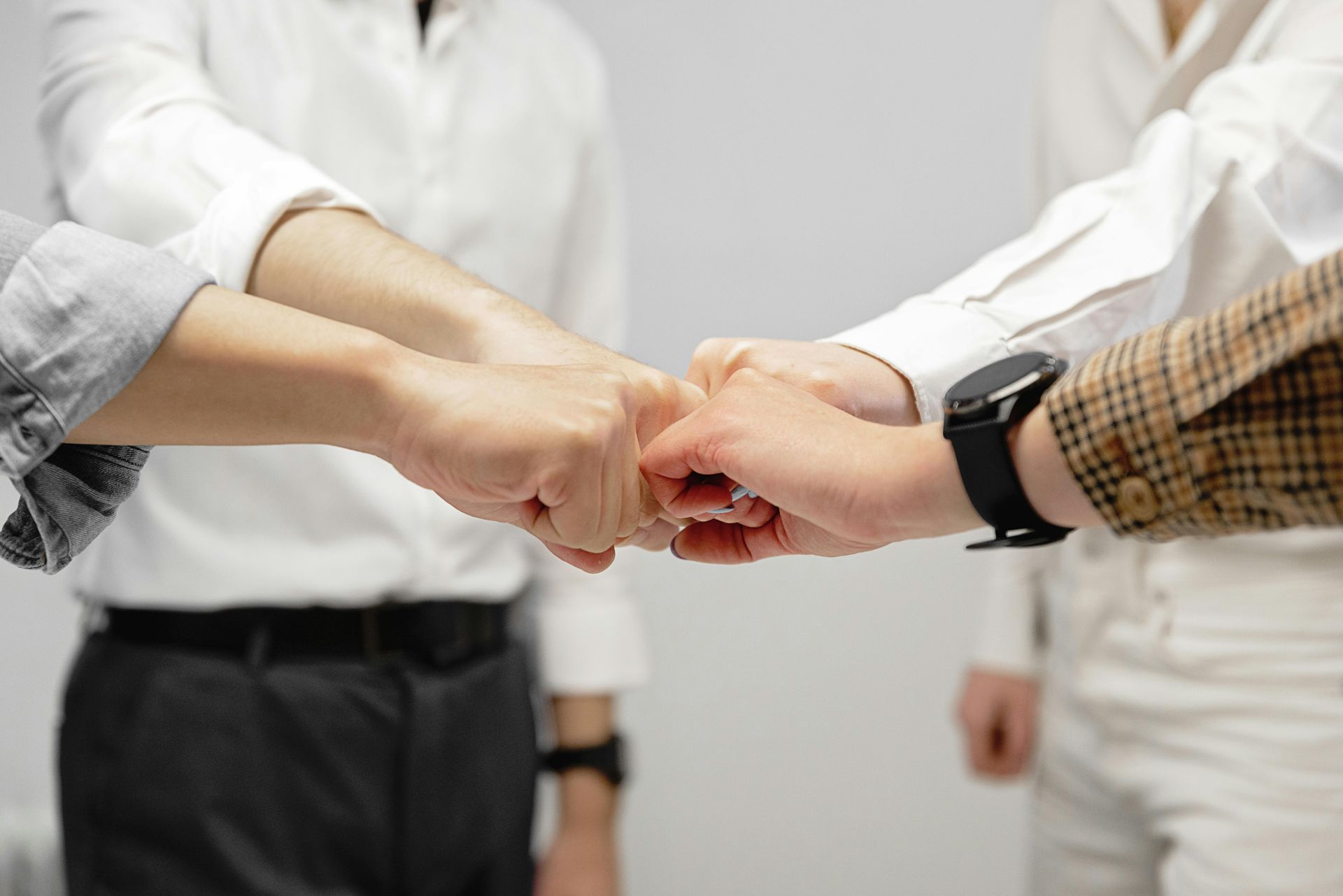 Four people in business attire bump fists, symbolizing teamwork and agreement.