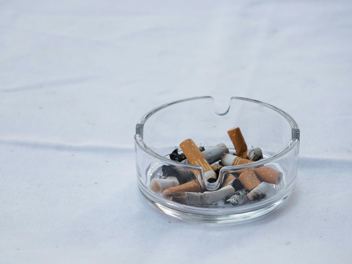 Glass ashtray with cigarette butts on a white tablecloth.