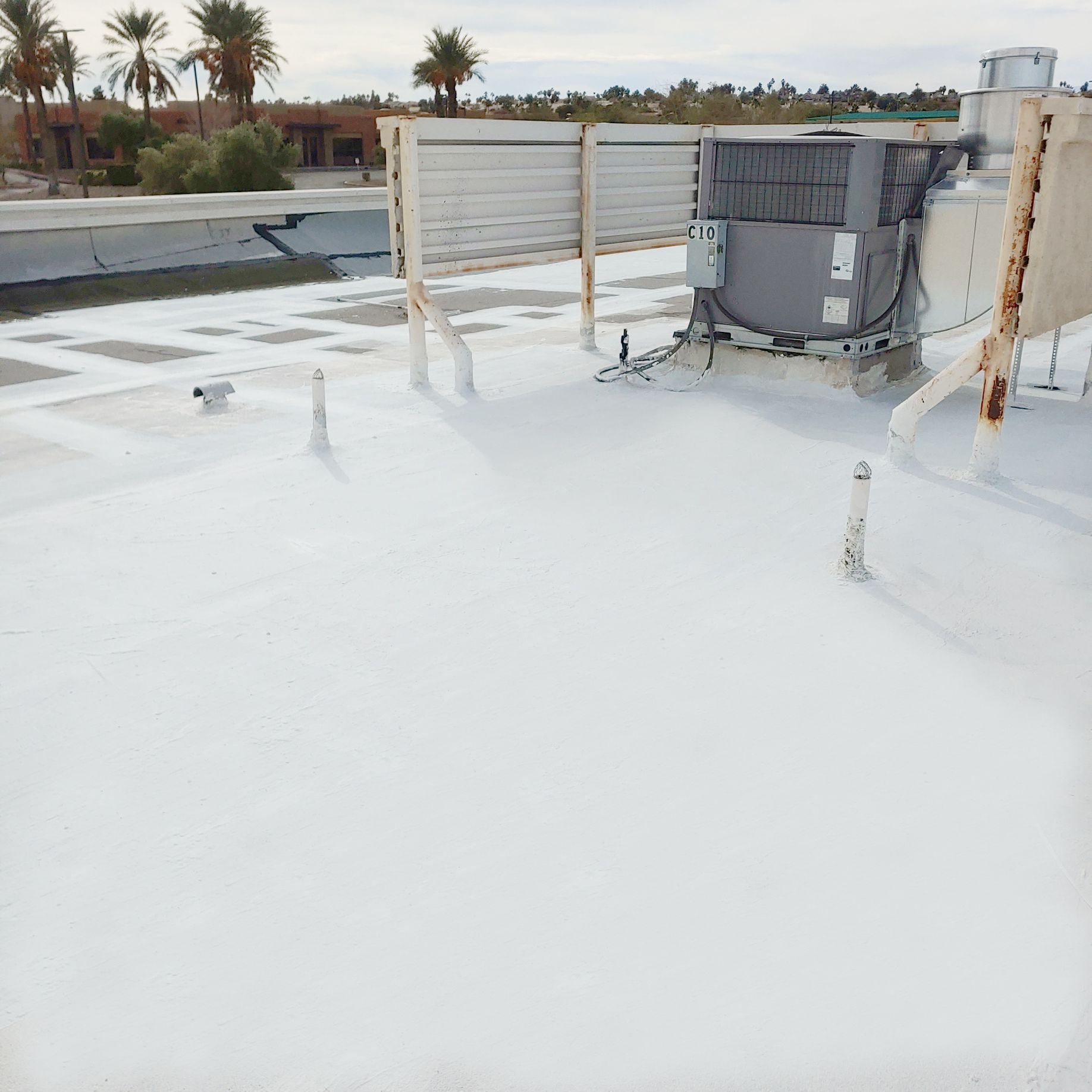 White coated flat roof with air conditioning unit, pipes, and desert landscape in the background.