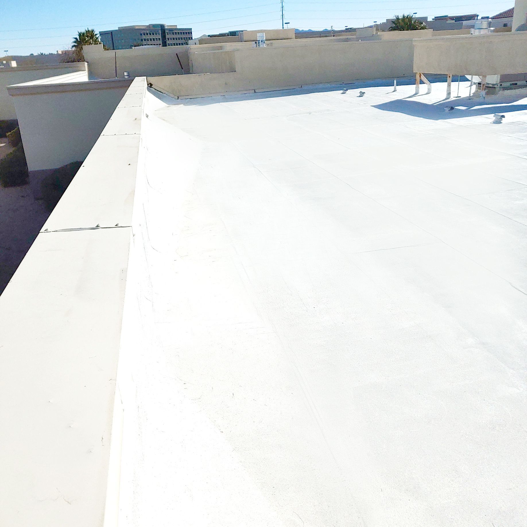 White flat roof with a low wall in the foreground, a building and blue sky in the background.
