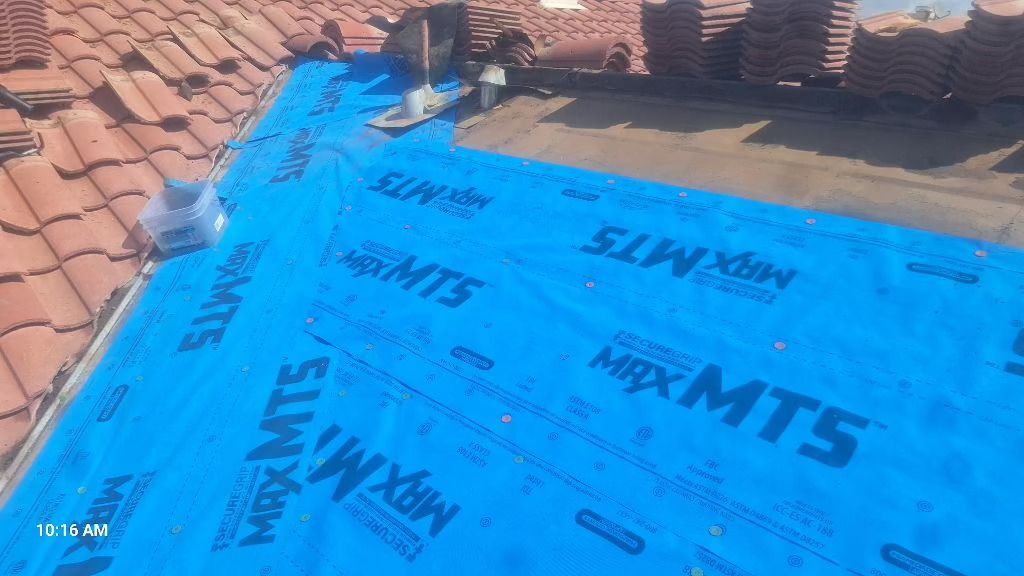 Roof with blue underlayment installed, surrounded by terracotta tiles and building materials.