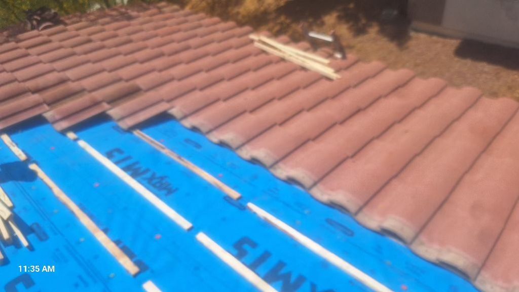 Roof being repaired with blue underlayment and red tiles.