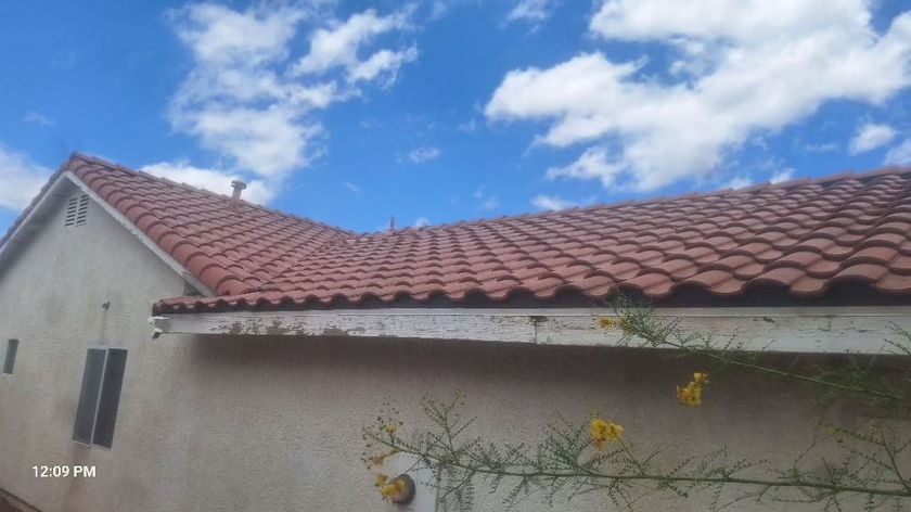 Red-tiled roof on a stucco house against a bright blue sky with scattered clouds.