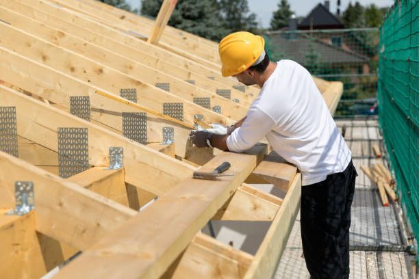 Construction worker building wooden roof frame wearing yellow hard hat under sunny sky outdoors.