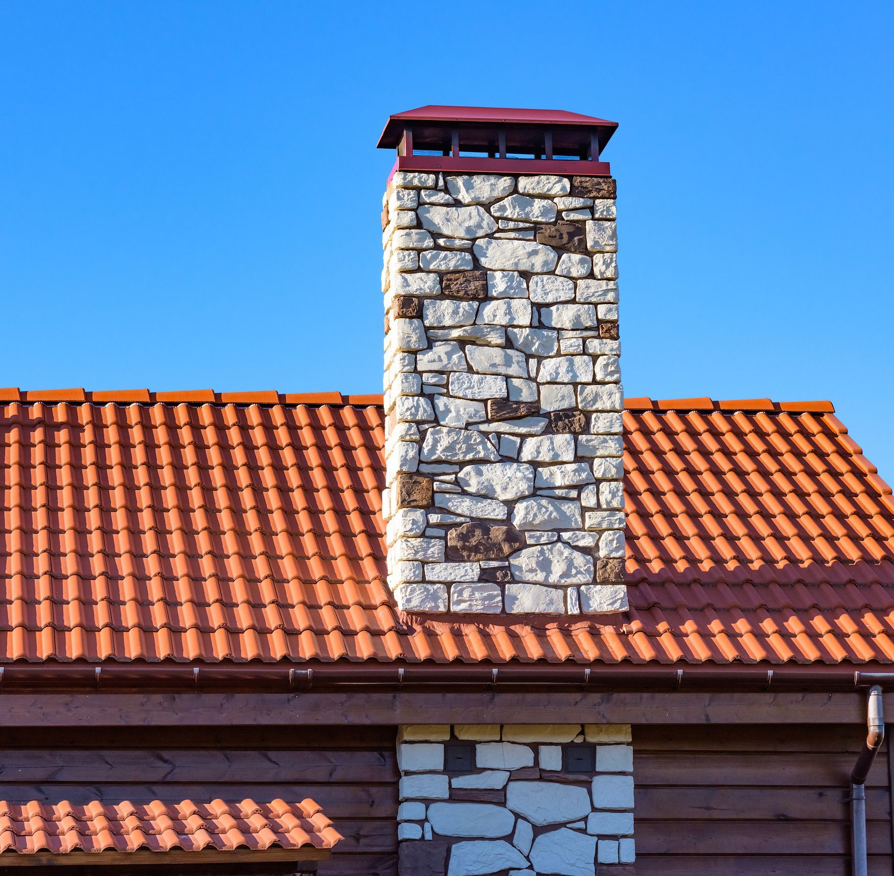 Brick chimney on a red-tiled roof against a bright blue sky.