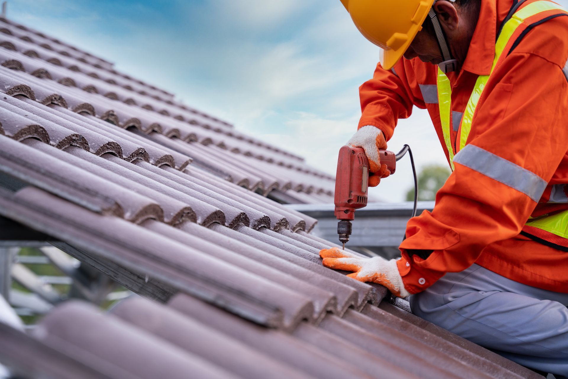 Roofing contractor installing tile roof with power drill during professional roof repair work today.