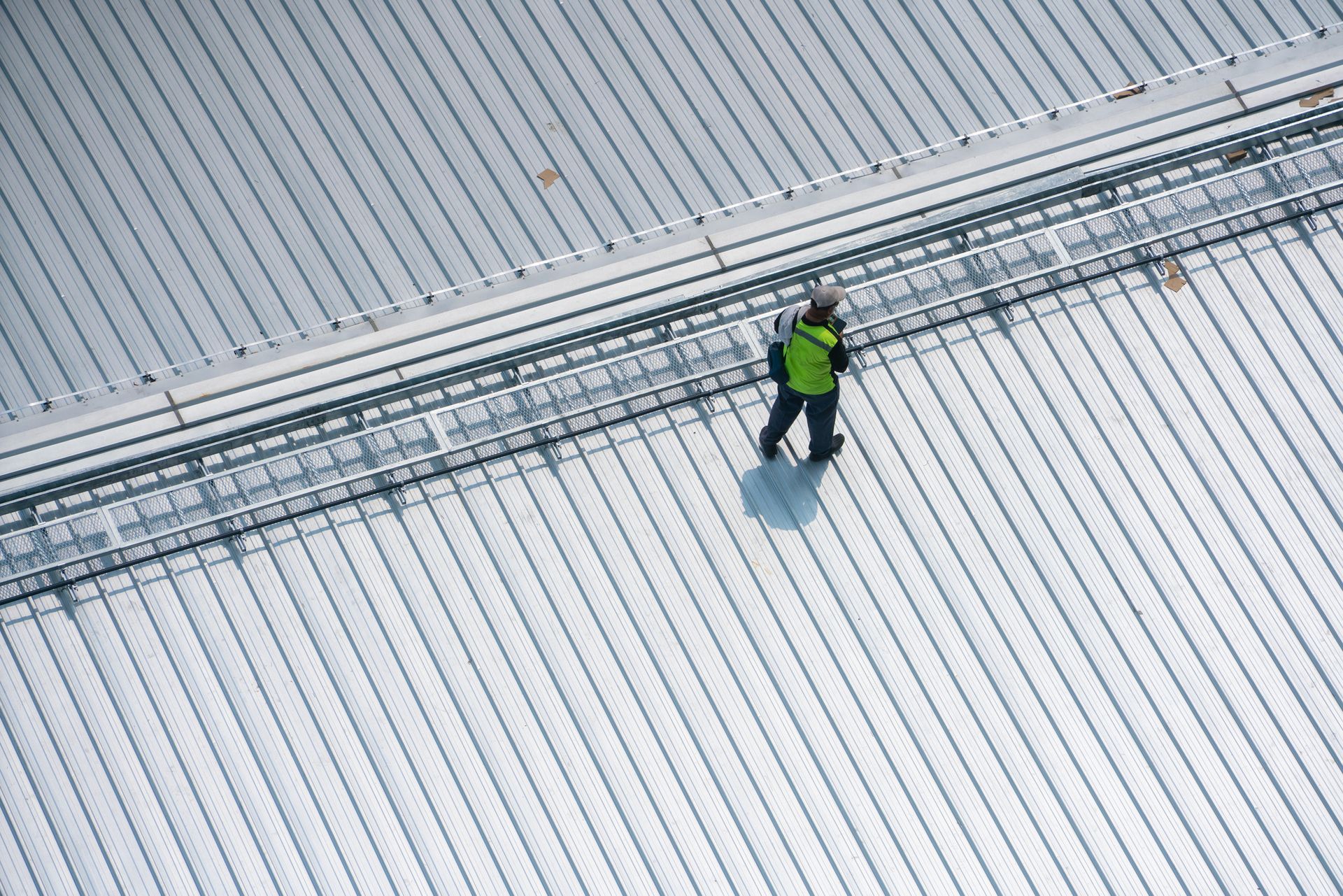 Roofer removing asphalt shingles from a roof with a shovel, wearing gloves, jeans, and knee pads.