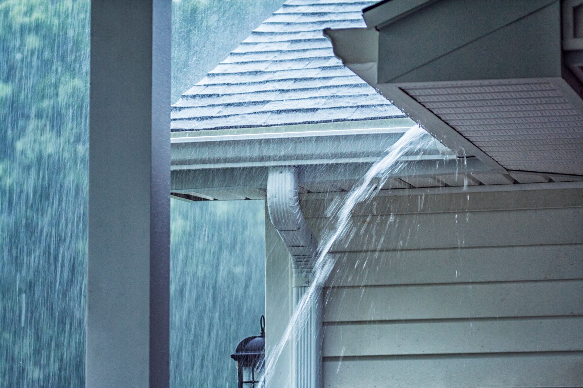 Rain pouring from a white house gutter during a storm.