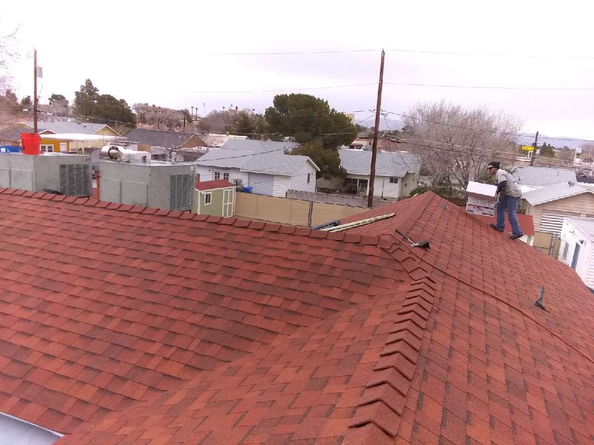 A person working on a tiled roof covered with a plastic tarp, near a chimney and solar panels.