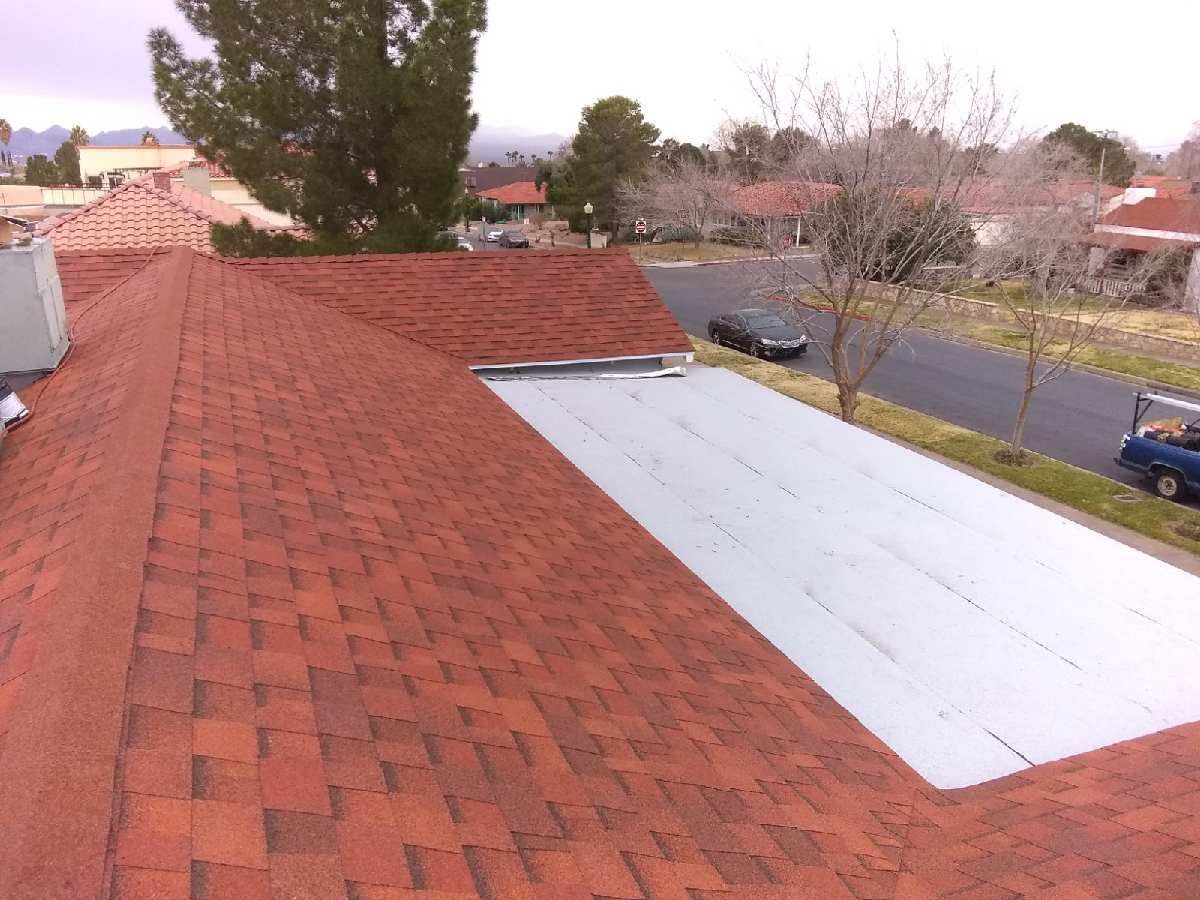Red shingle roof with a flat, white section. Houses and a street are in the background.